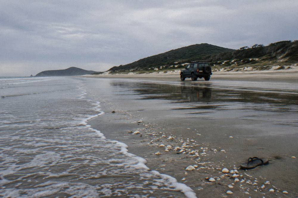 A four wheel drive vehicle travelling on firm wet sand along a long empty beach at low tide