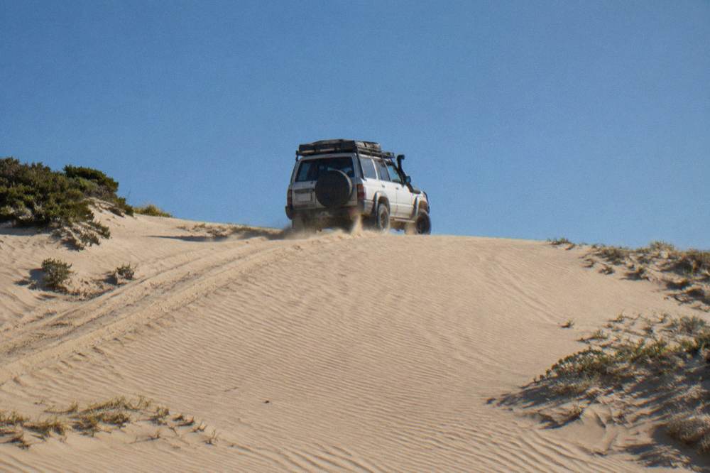 A guided four wheel drive tour vehicle cresting a steep sand dune under a clear sky