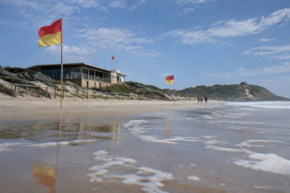 Red and yellow patrol flags standing on a wide sandy beach with a surf club building behind