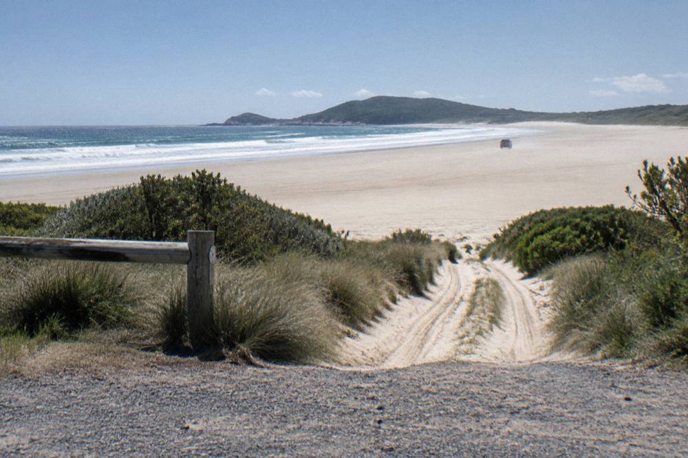 A permit sign beside a sandy track leading onto a wide beach