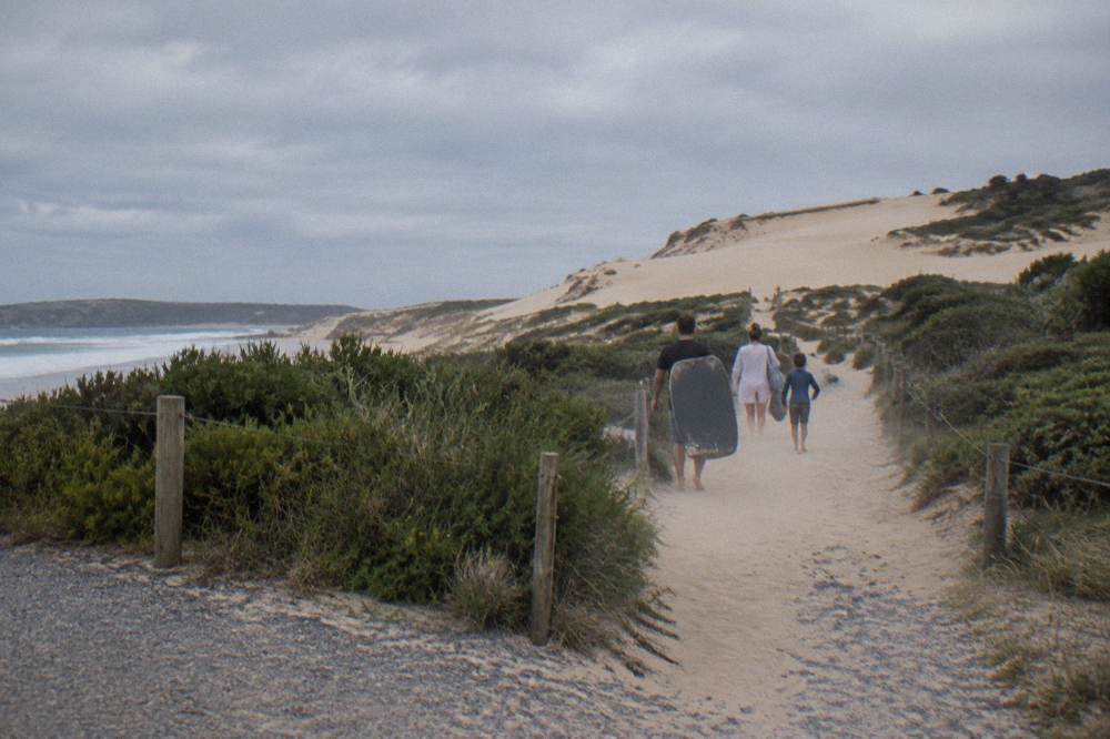 Visitors on foot at the base of tall sand dunes near a beach entrance track