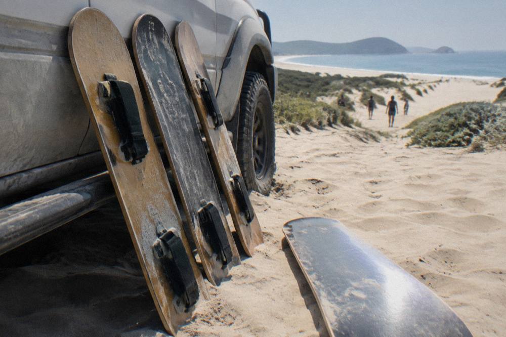 Rows of sandboards leaning against a 4WD vehicle parked on the dunes