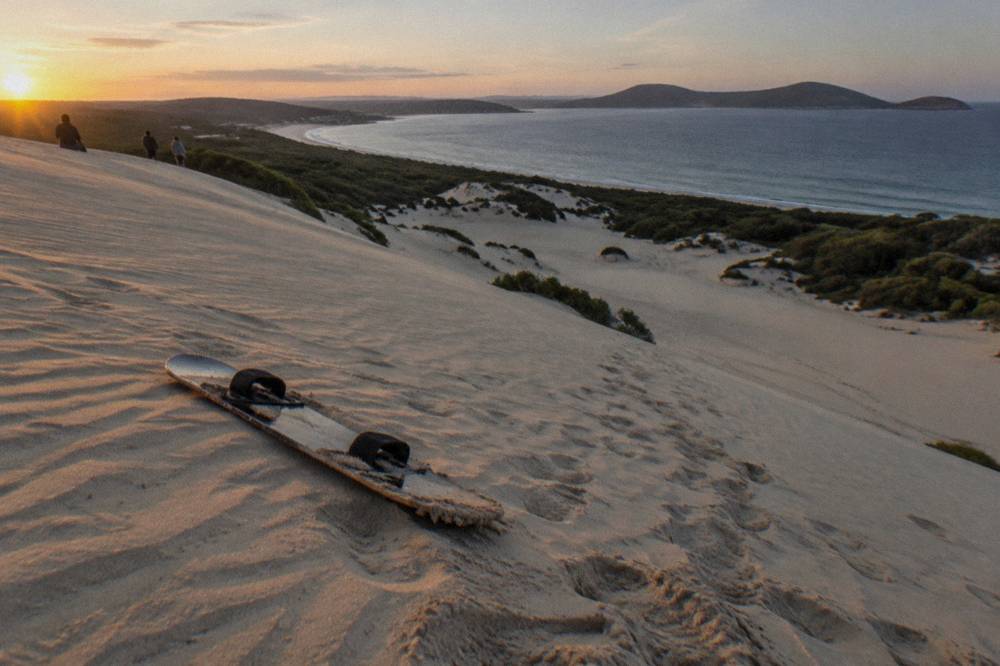 A sandboard resting on the smooth slope of a large coastal sand dune