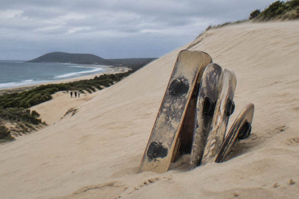 A small group of sandboards leaning against the base of a tall sand dune