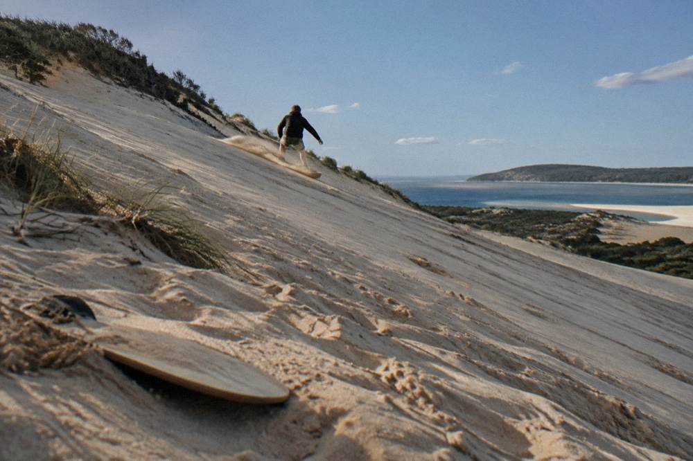 A sandboarder sliding down a steep sand dune at Anna Bay