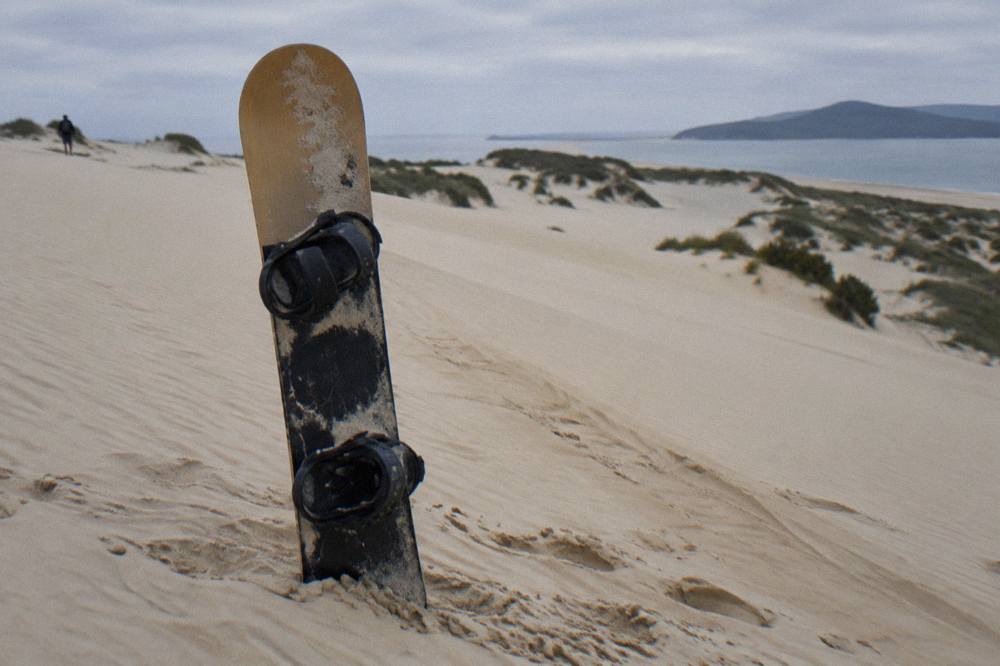 A sit-down sandboard resting on a smooth sand slope with dune ridges behind it