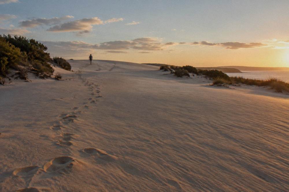 A line of footprints climbing a sand slope toward a wide dune ridge