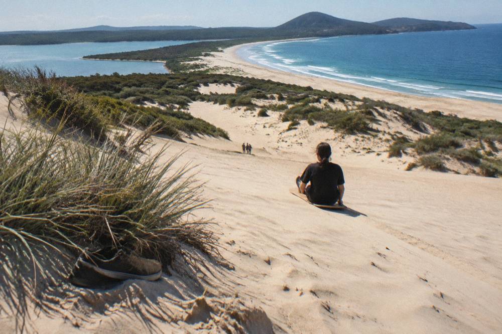 A rider sliding seated down a steep sand slope leaving a thin trail in the sand