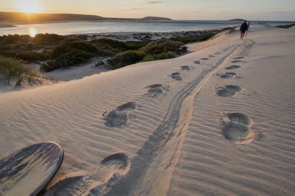 Footprints and a slide mark crossing a pale sand dune slope in late afternoon light