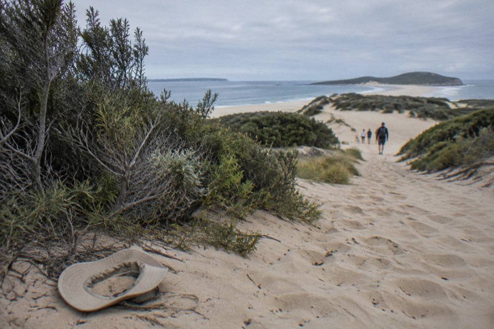 Footprints crossing a broad slope of pale sand toward distant dune ridges
