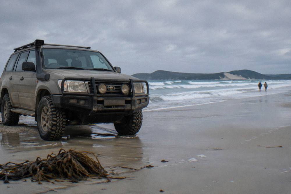 A four wheel drive vehicle parked on firm wet sand beside rolling surf