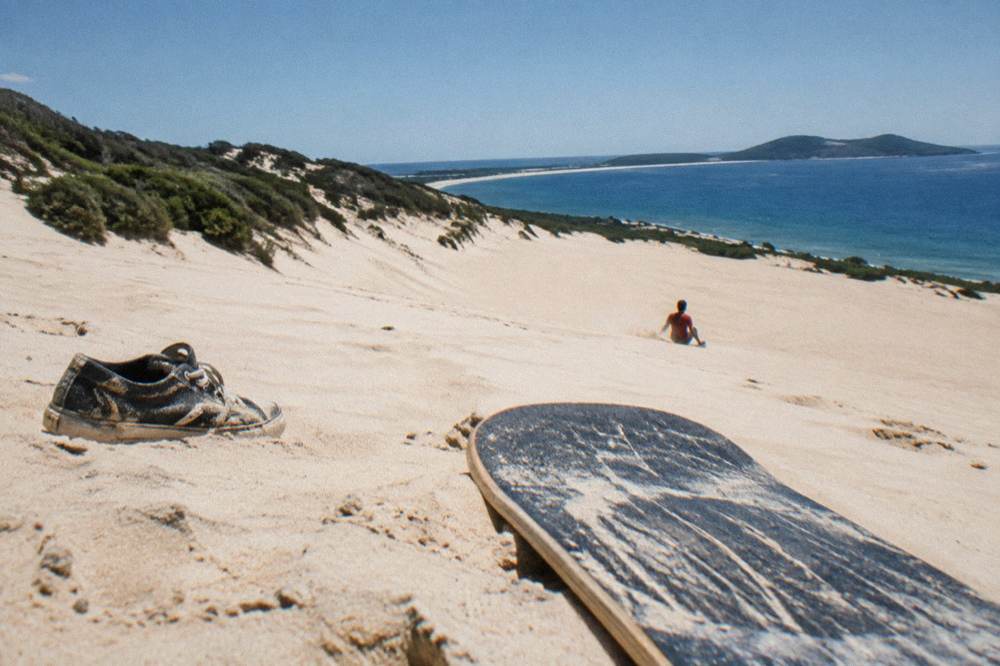 A person on a sandboard sliding down a smooth dune face