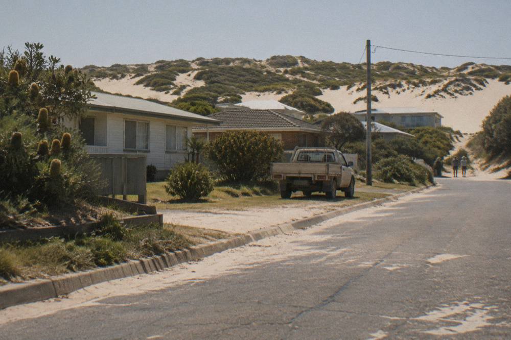 Sand dunes rising behind a quiet coastal town street with a view to the ocean