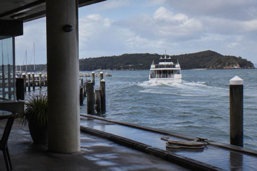 A tour boat leaving a marina in a sheltered harbour lined with headlands