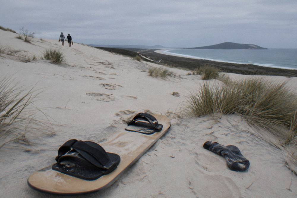 A sit-down sandboard lying face-up on pale dune sand with footprints trailing up the slope