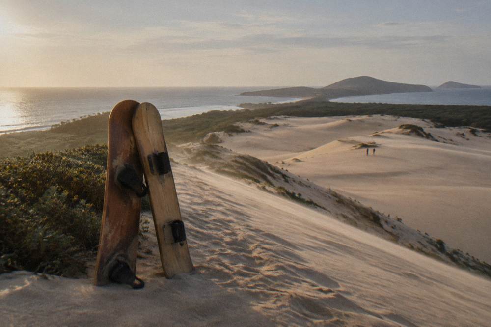 Two sandboards resting against each other on a dune crest with a wide sand field behind them
