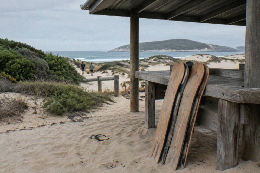 A shaded picnic area with boards stacked against a table on the edge of a sand dune