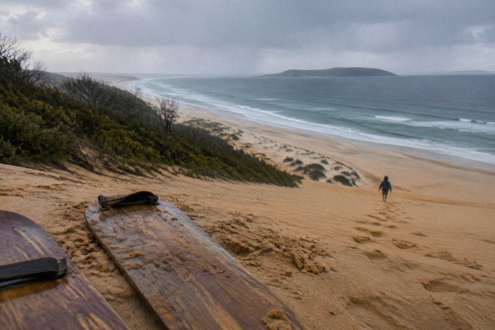 A sand slope with boards resting on the sand and a wide view over dunes to the sea