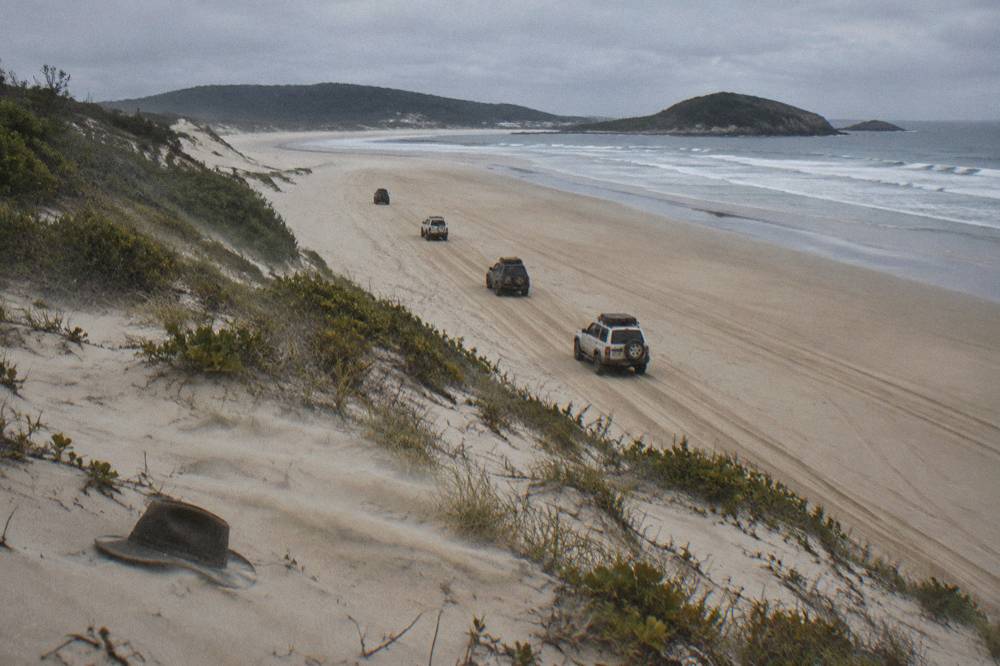 A convoy of four wheel drive vehicles following each other in tyre tracks along a broad flat beach
