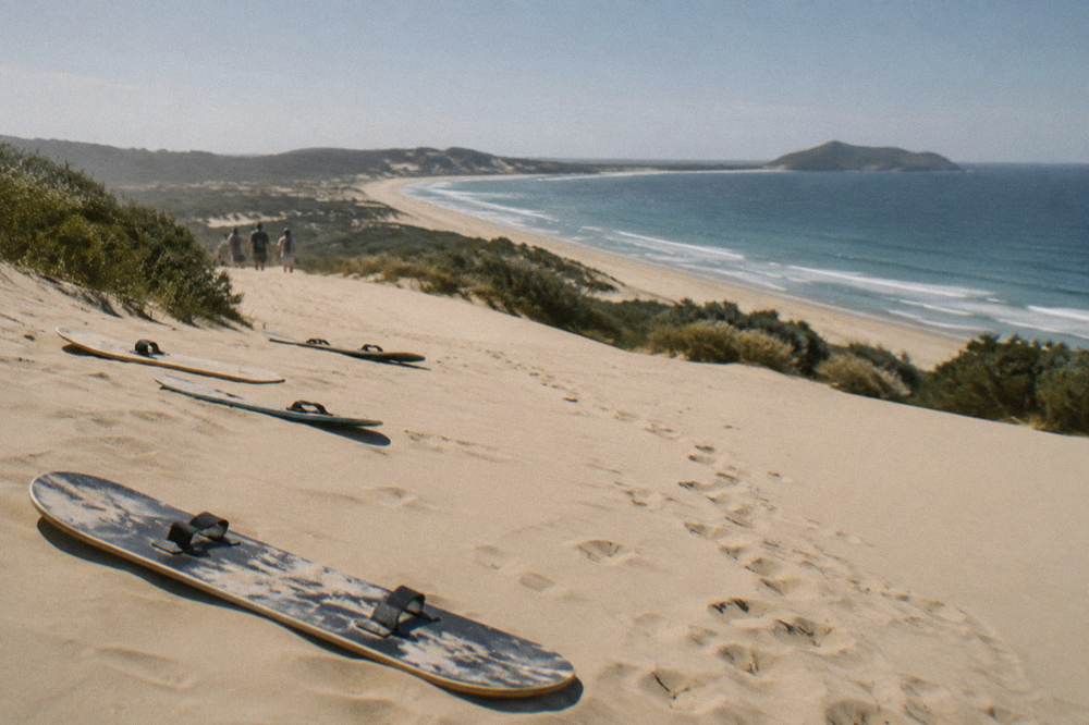Sandboards lying flat on a smooth sand slope above a wide empty beach at midday