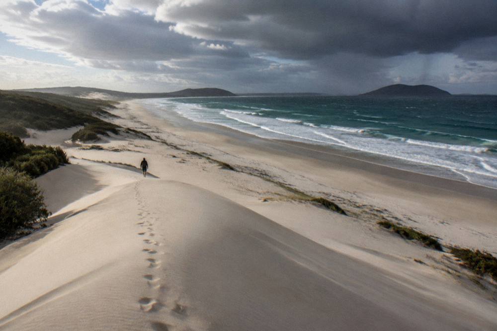 Wide view of tall pale sand dunes meeting a long empty beach under scattered clouds