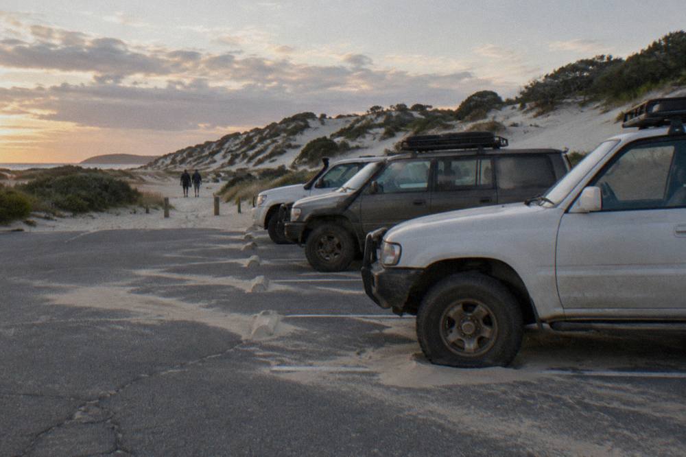 A line of four wheel drive vehicles parked on firm sand beside tall dunes