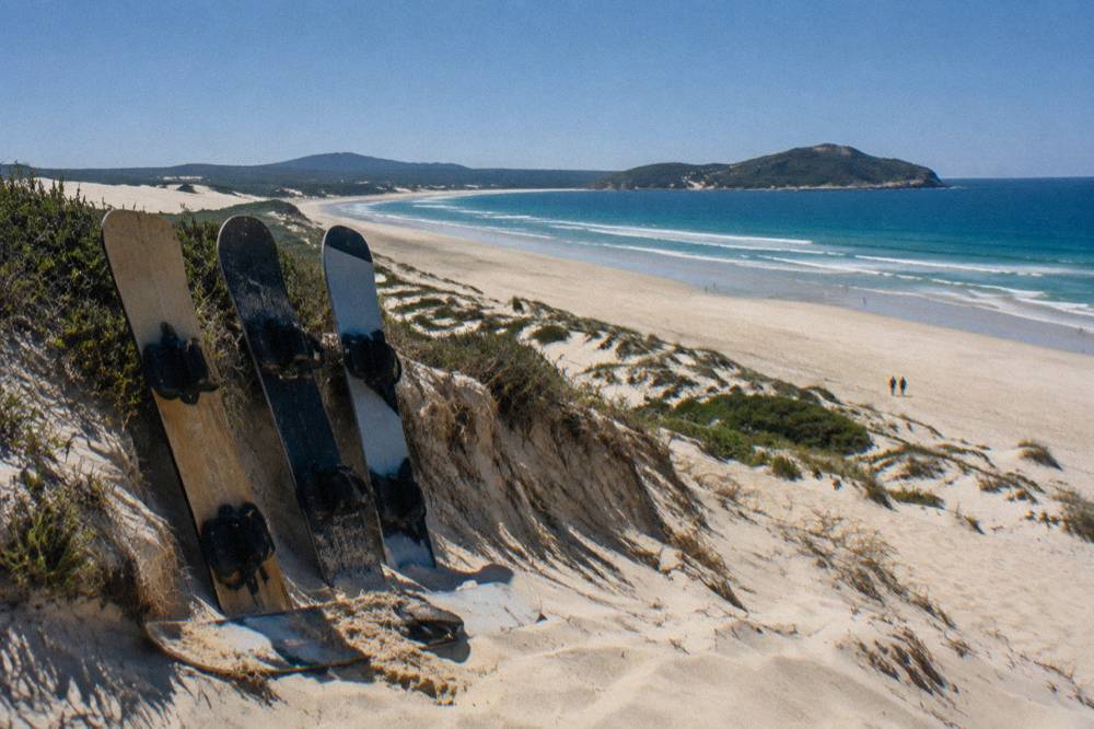 Sandboards leaning against a dune ridge above a wide flat beach at midday