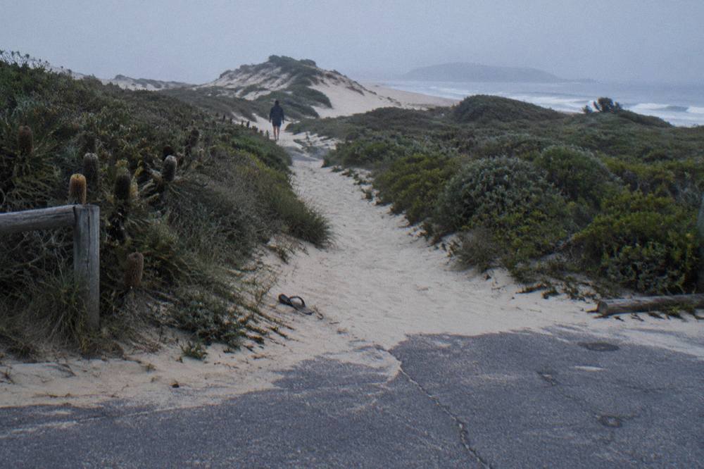 A sandy footpath leading from a beach car park toward tall dunes under an open sky