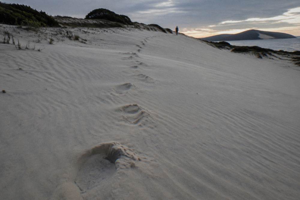 Footprints crossing a broad sand dune face toward a distant ridgeline of dunes