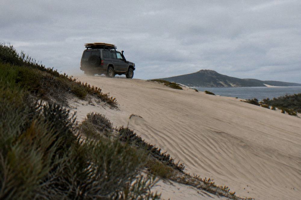 A four-wheel-drive vehicle on a sand dune with boards stacked on its roof rack