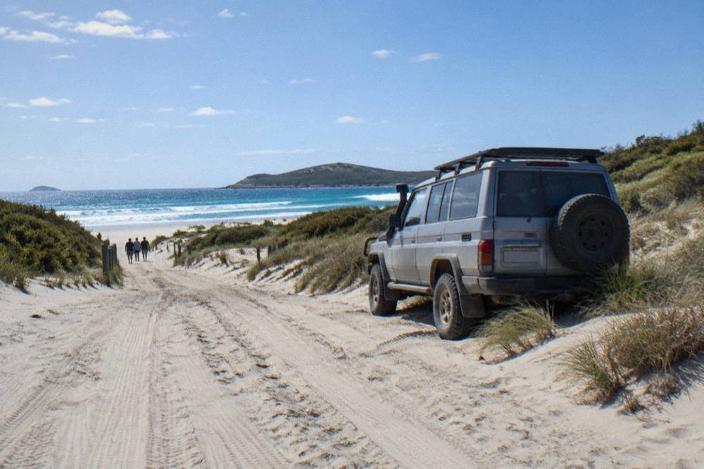 A four wheel drive vehicle parked on a broad sand track beside coastal dunes