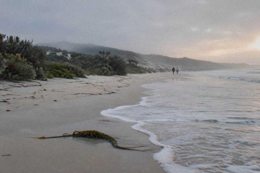 A white beach with gentle surf and a line of low coastal scrub