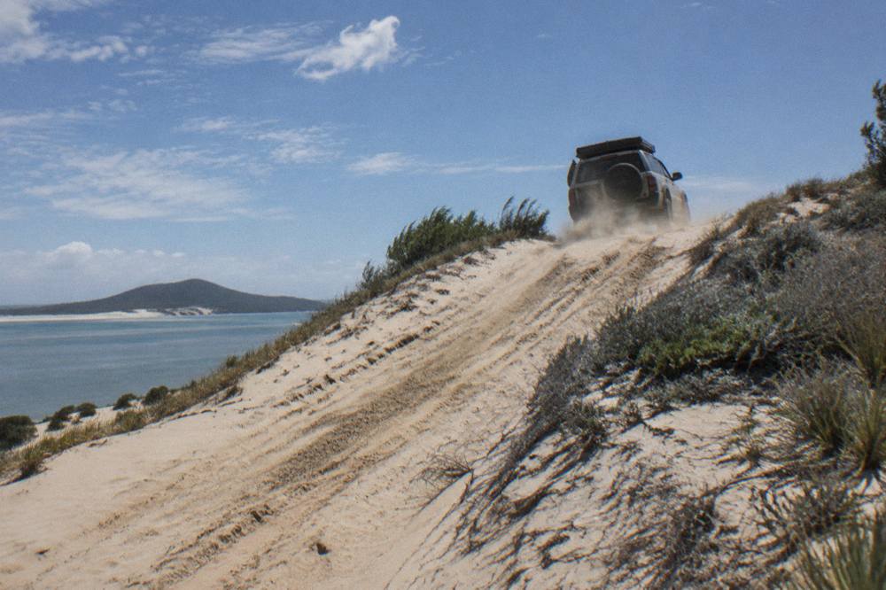 A four wheel drive vehicle climbing a steep golden sand dune under an open sky