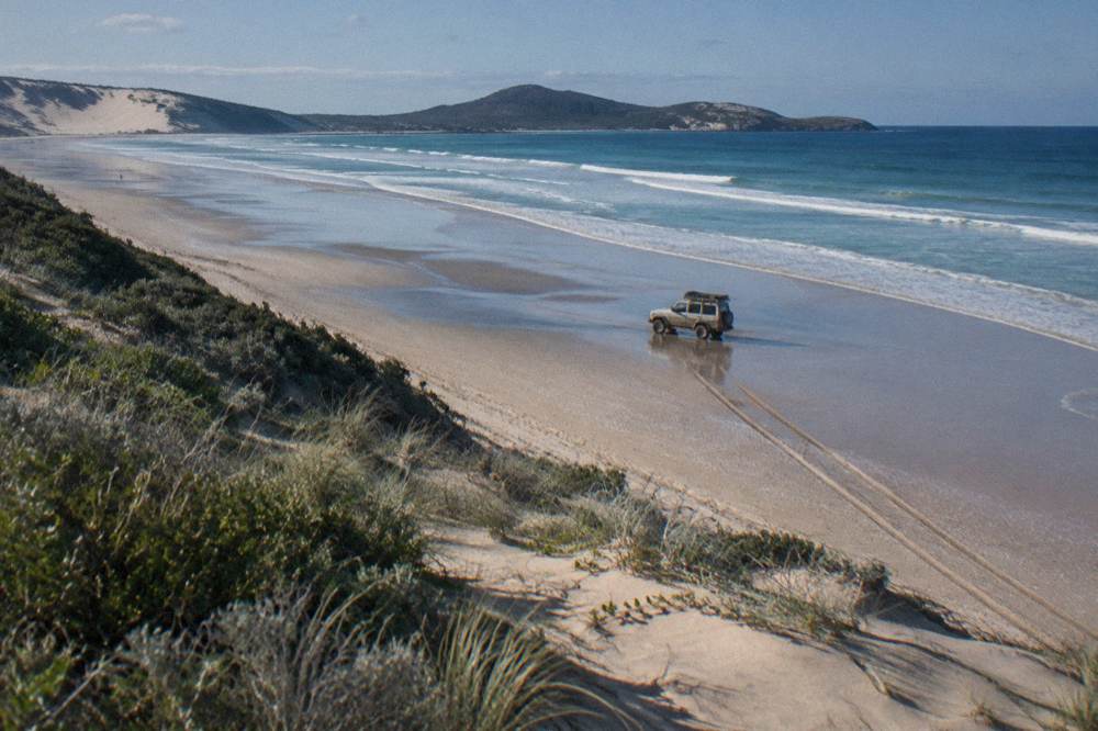 A four wheel drive tour vehicle parked on firm wet sand at the waterline of a long beach