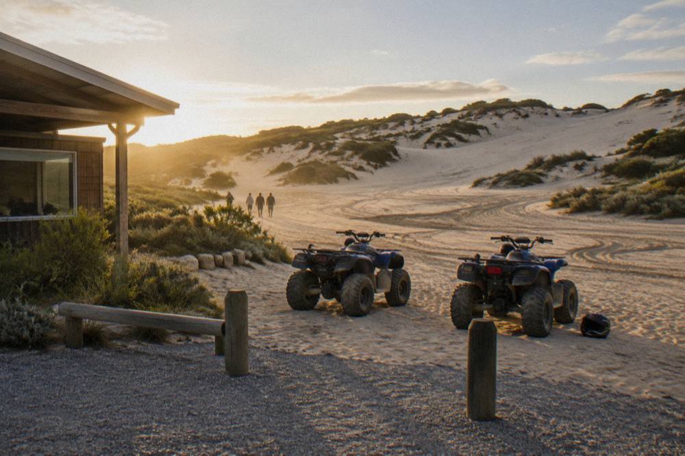 Sand dunes rising above a stretch of beach with vehicle tracks in the sand