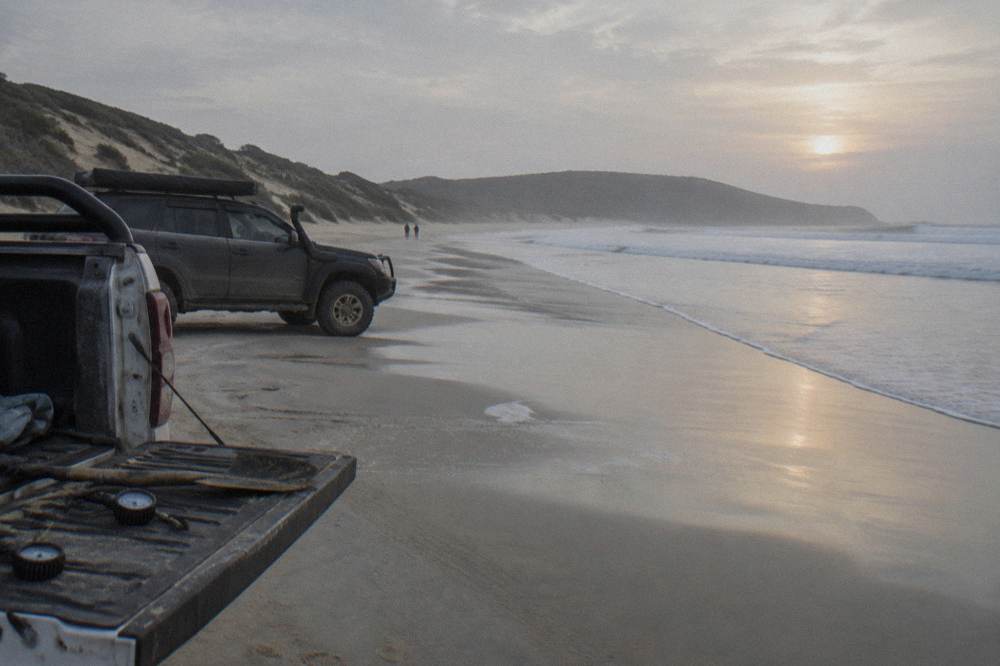 Four wheel drive vehicles parked on firm wet sand beside rolling dunes