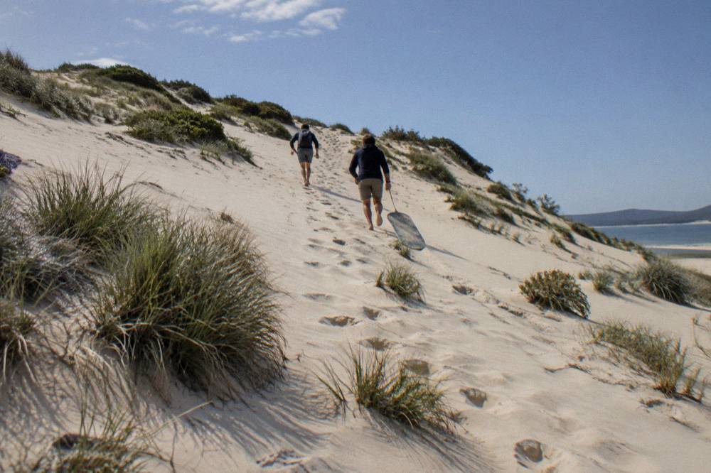 People walking up a pale sand slope under a clear sky