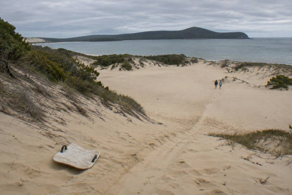 A gentle sand slope with a worn sliding track running down to a flat sandy basin