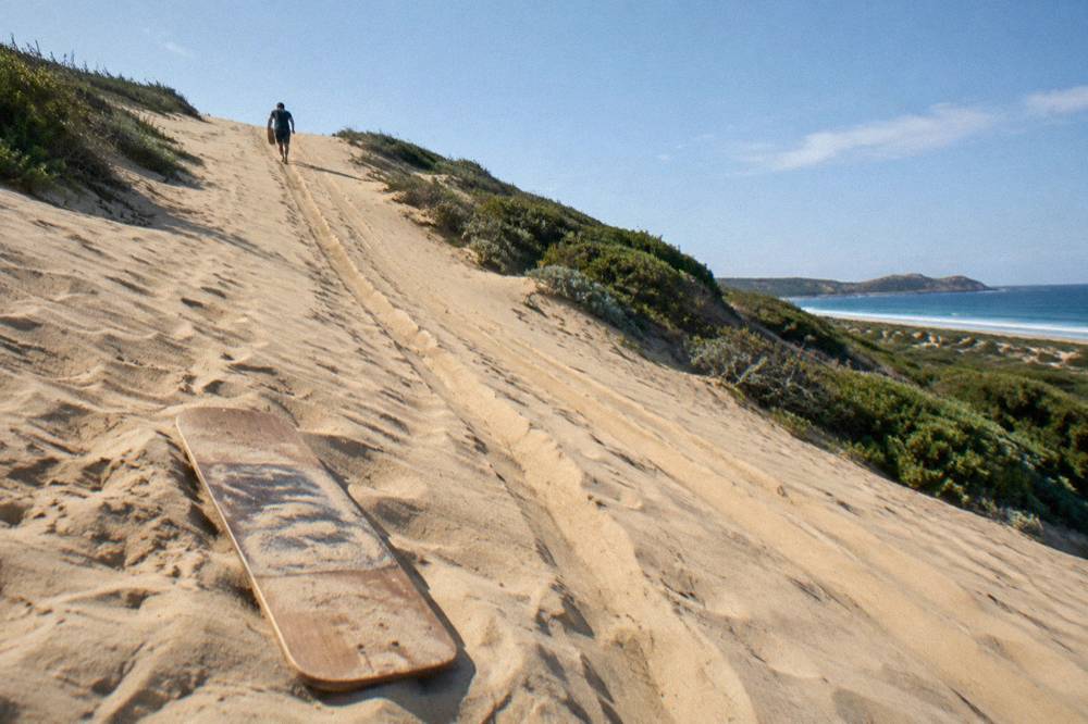 A sandboard resting on a smooth dune slope above the beach