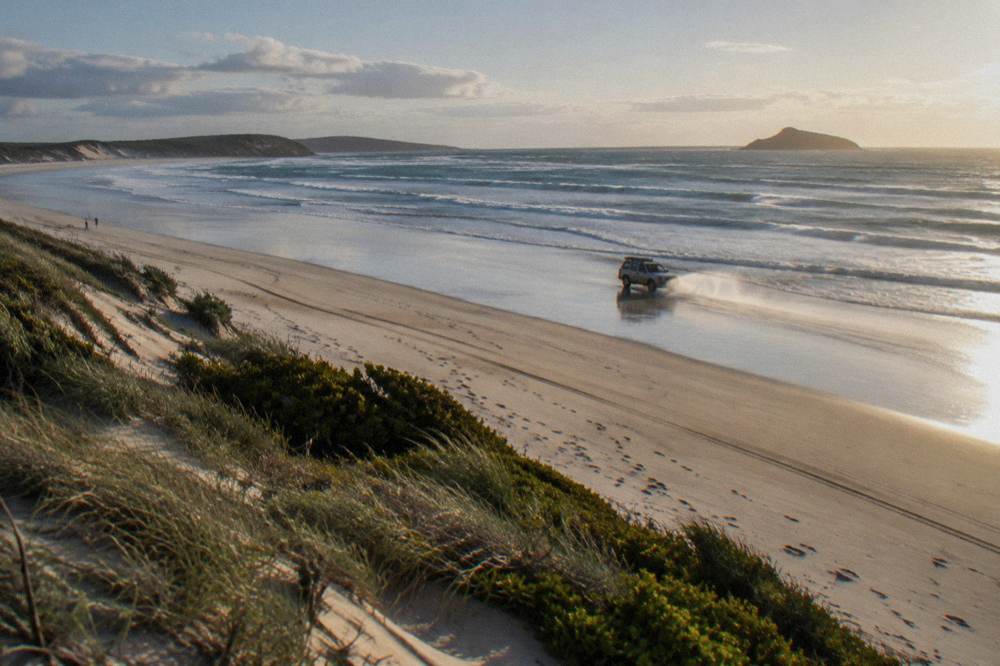 A four-wheel drive vehicle travelling along wet sand at the water's edge