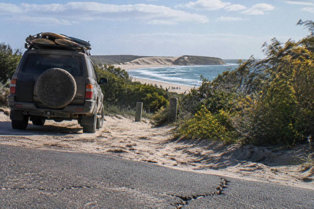 A four wheel drive vehicle on sand with boards loaded for a dune session