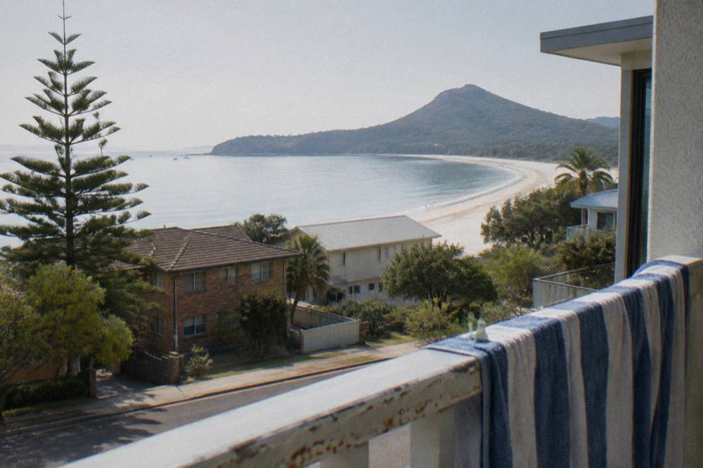 Low-rise coastal buildings above a curved bay beach with calm water