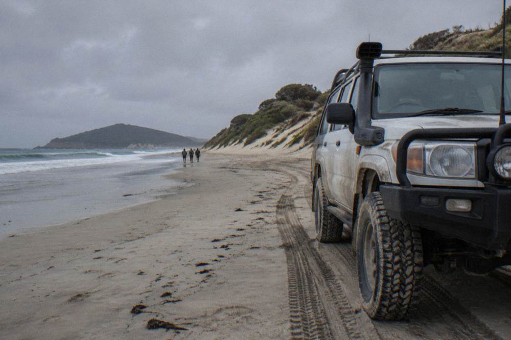 A four wheel drive vehicle parked on firm sand near the base of tall dunes